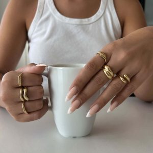 Woman wearing multiple stylish rings, including the Adi Ring, while holding a white mug.