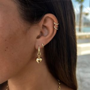 Close-up of a woman wearing Amy Heart Earrings with a balloon heart charm, showcasing stylish gold hoops.