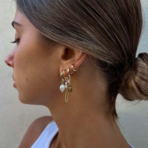 Close-up of a woman wearing Bar Earrings Set featuring gold hoops, pearls, and charms in an asymmetrical design.