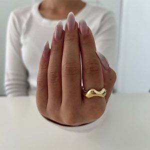 A hand displaying the Dani Ring with smooth, flowing curves, showcasing a bold and trendy gold design.