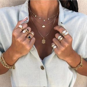 Stylish woman wearing multiple rings including a bold Drop Ring, layered necklaces, and gold bracelets.