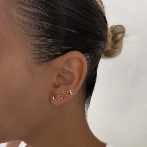 Tiny Initial Earring worn on ear, showcasing gold letters spelling 'LOVE' for a personalized jewelry style.