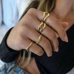 Liquid Ring worn with other golden statement rings on a model's hand against a blurred background.