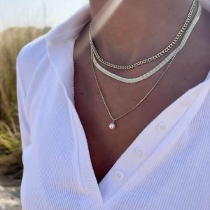 Close-up of a person wearing the Mari Necklace with a smooth chain and round pearl, styled elegantly with a white shirt.
