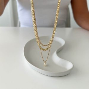 Mari Necklace Set displayed elegantly with layered gold chains and a pearl pendant on a minimalist plate.