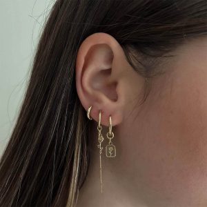 Close-up of a woman's ear showcasing the delicate Marilyn Earrings with golden hoops and hanging chains.