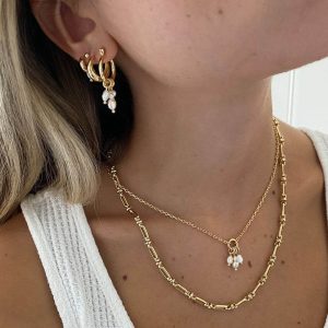 Model wearing Monaco Earrings with pearl drops and layered gold necklaces for an elegant look.