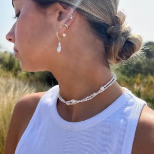 Model wearing Praline Earrings with pearls and a chic hairstyle in a sunny outdoor setting.